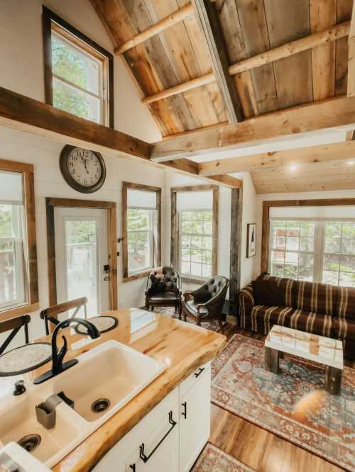 Cozy interior of a rustic cabin with wooden beams, a clock, and a comfortable seating area by large windows.