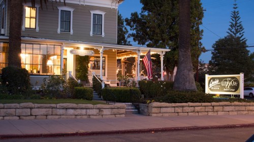 A charming historic building at dusk, featuring warm lights, a welcoming porch, and a sign for "Uptown Inn & Cottage."