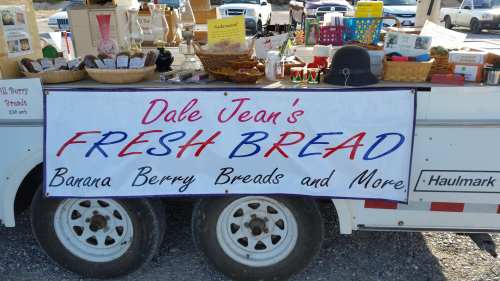 A vendor's cart displaying a sign for "Dale Jean's Fresh Bread" with various baked goods and crafts.