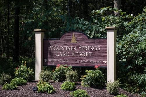 Sign for Mountain Springs Lake Resort, featuring directions to the office, chicken, and the lodge restaurant, surrounded by greenery.