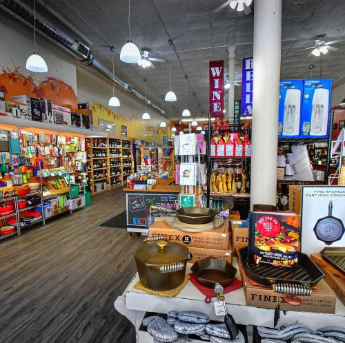 A colorful retail store interior filled with kitchenware, wine, and various home goods, with bright lighting and shelves.