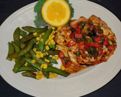 Grilled chicken topped with salsa, served with green beans, corn, and a lemon slice on a white plate.
