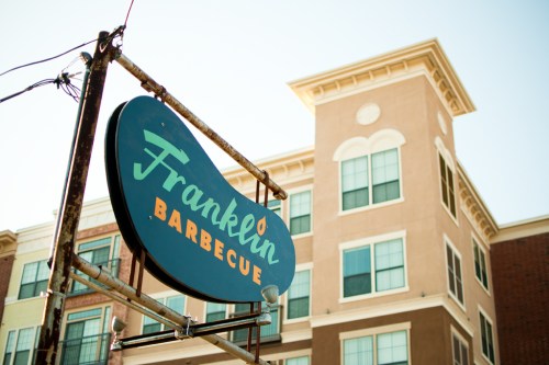 Sign for Franklin Barbecue in front of a multi-story building, with clear blue skies above.