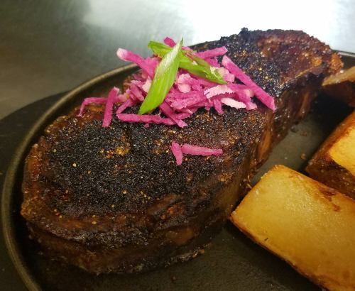 A seared piece of meat topped with pink pickled onions and green onions, served with golden roasted potatoes.