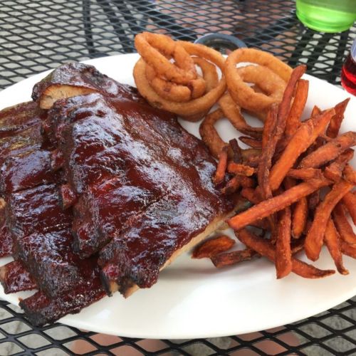 A plate of barbecue ribs with a glossy sauce, served with sweet potato fries and onion rings.