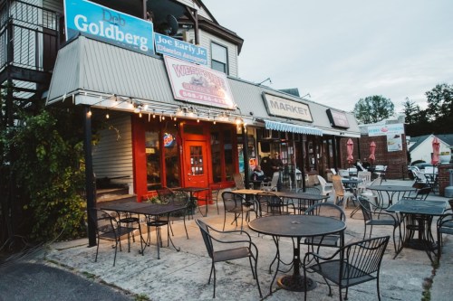 A quaint market with outdoor seating, illuminated by string lights, in a small town setting during dusk.