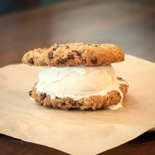 A chocolate chip cookie sandwich filled with vanilla ice cream, resting on a piece of parchment paper.