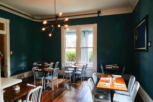 A cozy restaurant interior with teal walls, wooden tables, and modern light fixtures, featuring several empty chairs.