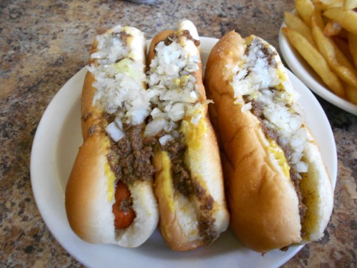 Three hot dogs topped with chopped onions and ground beef, served on a plate with a side of fries.