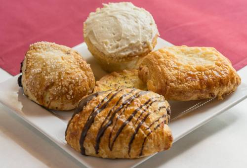 A plate of assorted pastries, including a muffin, croissant, and sweet rolls, on a red tablecloth.