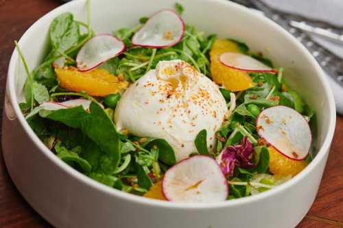 A fresh salad with greens, orange segments, radish slices, and a poached egg on top, garnished with spices.