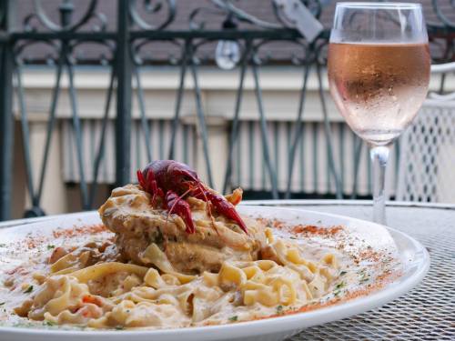 A plate of creamy pasta topped with a crawfish, alongside a glass of rosé wine on a table.