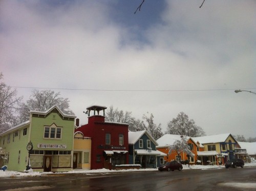 Colorful buildings line a snowy street under a cloudy sky, creating a charming winter scene.