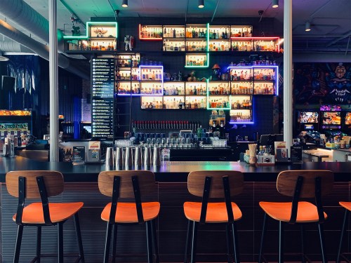 A modern bar with colorful shelves of liquor bottles and empty stools lined up at the counter.