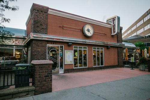 A retro-style diner with a brick exterior and large windows, featuring a vintage sign and outdoor seating.