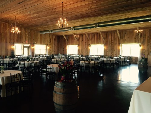 A spacious wooden venue with chandeliers, tables set for an event, and large windows letting in natural light.