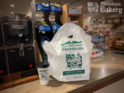 A takeout bag and coffee cup from Das Dutchman Essenhaus Bakery on a counter with food service equipment in the background.