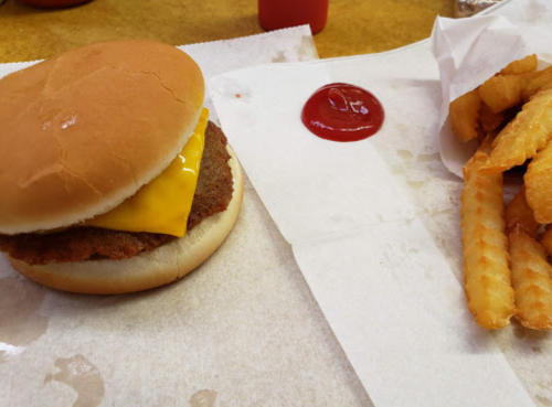 A cheeseburger with a slice of cheese and a side of crinkle-cut fries with ketchup on a paper tray.