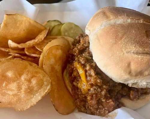 A hearty sandwich with ground beef and cheese, served with crispy potato chips and pickles on the side.