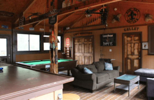 Cozy cabin interior featuring a pool table, sofa, and rustic decor with wooden walls and warm lighting.