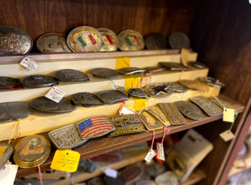 A display of various antique belt buckles on a wooden shelf, some with flags and decorative designs.
