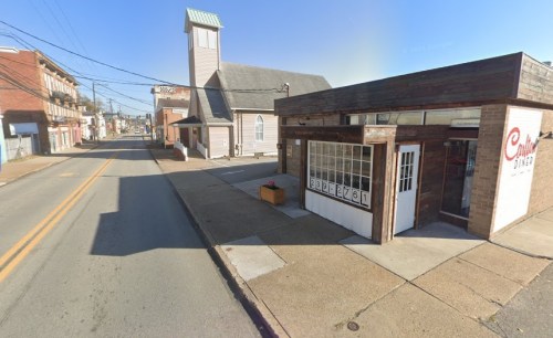 A street view featuring a diner and a church, with buildings lining the road under a clear blue sky.