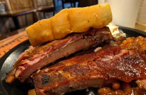 A plate featuring tender ribs topped with barbecue sauce, served with baked beans and a slice of bread.