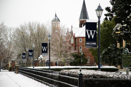 Snow-covered street with welcome banners, historic buildings, and lampposts in a winter landscape.