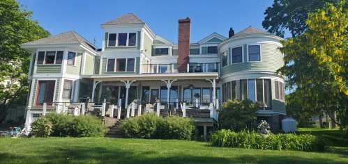 A large, green Victorian-style house with multiple gables and a spacious deck surrounded by greenery.