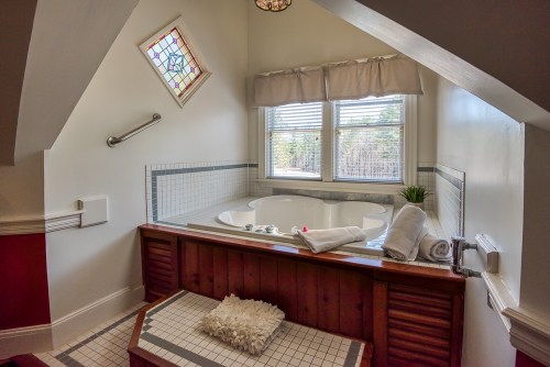 Cozy bathroom featuring a jetted tub, window with natural light, and decorative stained glass.