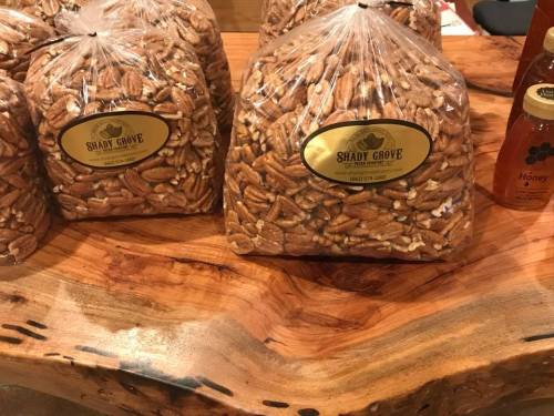 Bags of pecans labeled "Shady Grove" on a wooden table, with jars of honey in the background.
