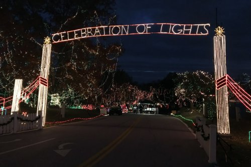 A festive archway reading "Celebration of Lights" above a road lined with colorful holiday lights.