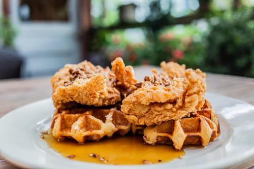 A plate of crispy fried chicken on top of golden waffles, drizzled with syrup, set against a blurred outdoor background.