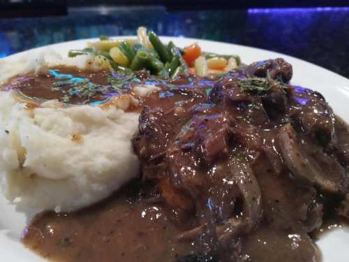 A plate of mashed potatoes topped with gravy, served with beef and mixed vegetables on the side.