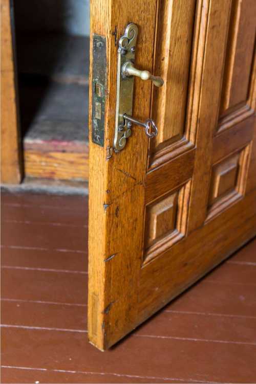 A partially open wooden door with intricate hardware, revealing a glimpse of a dimly lit interior.