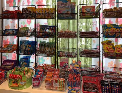 A colorful display of various candies and snacks in wire baskets against a floral backdrop.