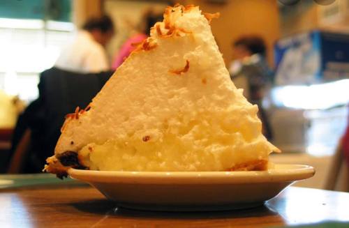 A slice of coconut cream pie with a fluffy meringue topping on a small plate, set on a wooden table.