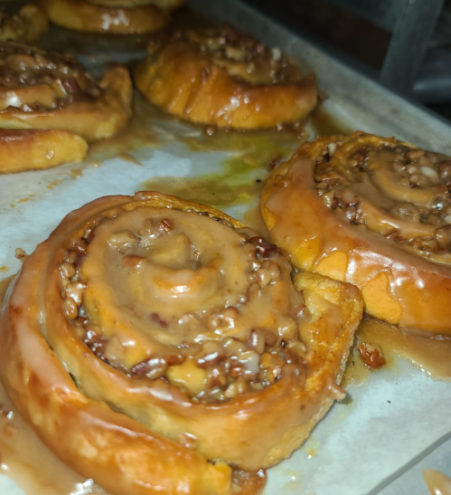 Freshly baked cinnamon rolls with a glossy caramel glaze and chopped nuts, resting on a baking tray.