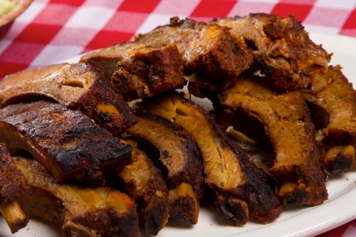 A plate of smoky, grilled ribs with a crispy exterior, served on a checkered tablecloth.