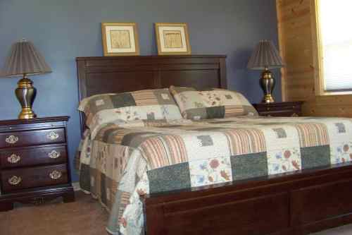 Cozy bedroom featuring a wooden bed, patterned quilt, nightstands, and lamps against a blue wall.