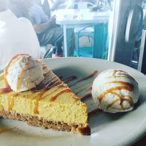 A slice of pumpkin cheesecake topped with whipped cream and caramel, served with two scoops of vanilla ice cream.
