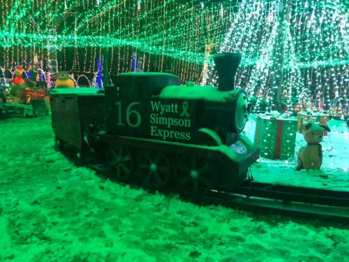 A decorated train named "Wyatt Simpson Express" surrounded by colorful lights and snow in a festive setting.