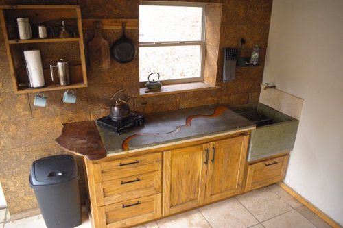 A modern kitchen with wooden cabinets, a stone countertop, and a window, featuring a sink and a gas stove.