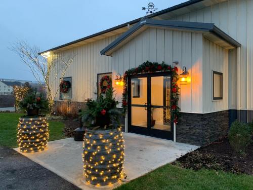 A festive building entrance decorated with wreaths and lights, featuring two planters with greenery and string lights.