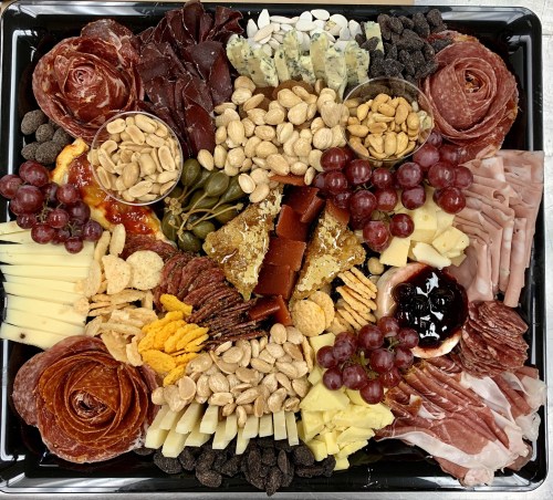 A colorful charcuterie board featuring meats, cheeses, nuts, fruits, and spreads arranged artfully.