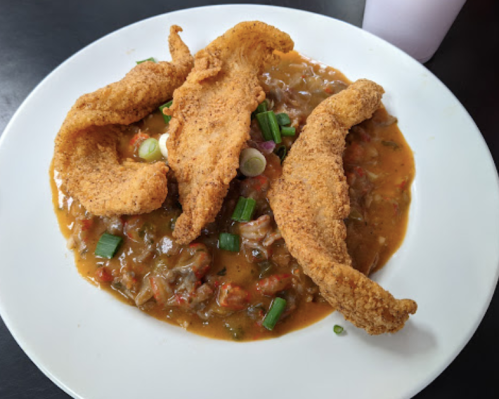 A plate of fried fish fillets served over a savory sauce with chopped green onions.