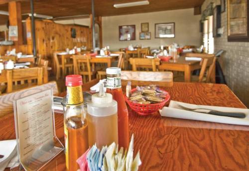 A cozy restaurant interior with wooden tables, condiments on a table, and a basket of utensils.