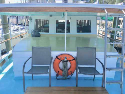 A boat's deck featuring two chairs, a life ring, and a view of the cabin area with large windows.