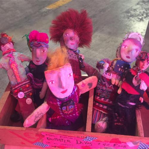 A colorful display of handmade dolls with unique hairstyles and outfits, arranged in a wooden box.