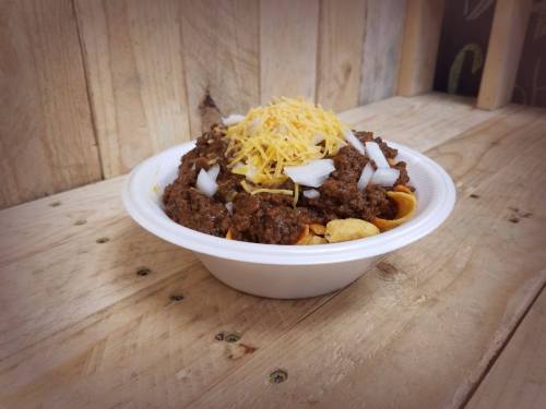A bowl of chili topped with shredded cheese and onions, served on a bed of corn chips, on a wooden surface.